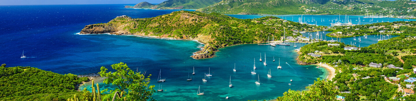 Das atemberaubende Luftbild zeigt die leuchtend grünen Landschaften von Antigua und Barbuda, umgeben vom tiefblauen Meer, in dem Boote malerisch verstreut sind.