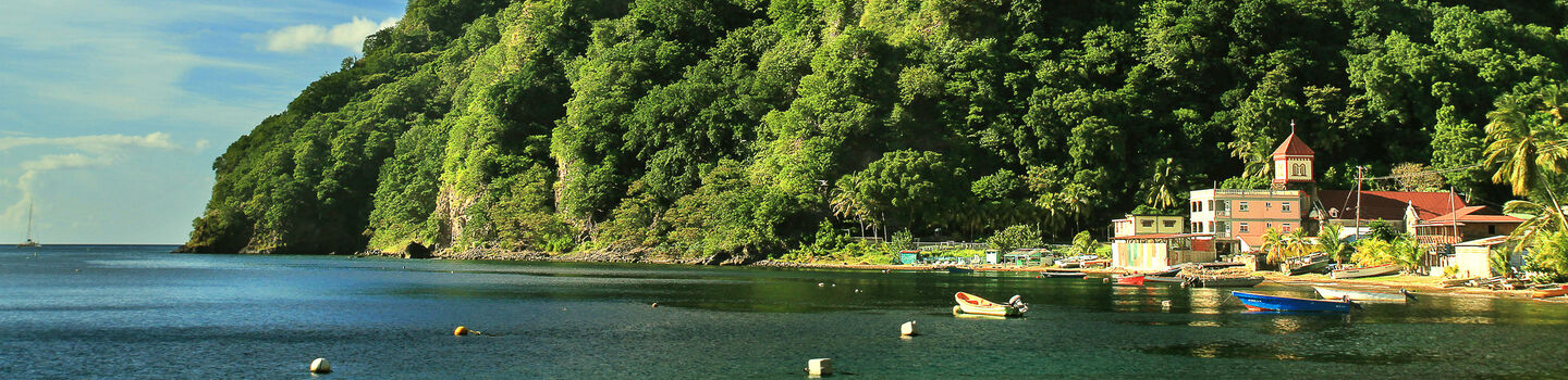 An einem von grünen Hügel gesäumten Ufer liegt ein beschauliches Fischerdorf, dessen Boote friedlich auf dem grünblauen Meer schaukeln.