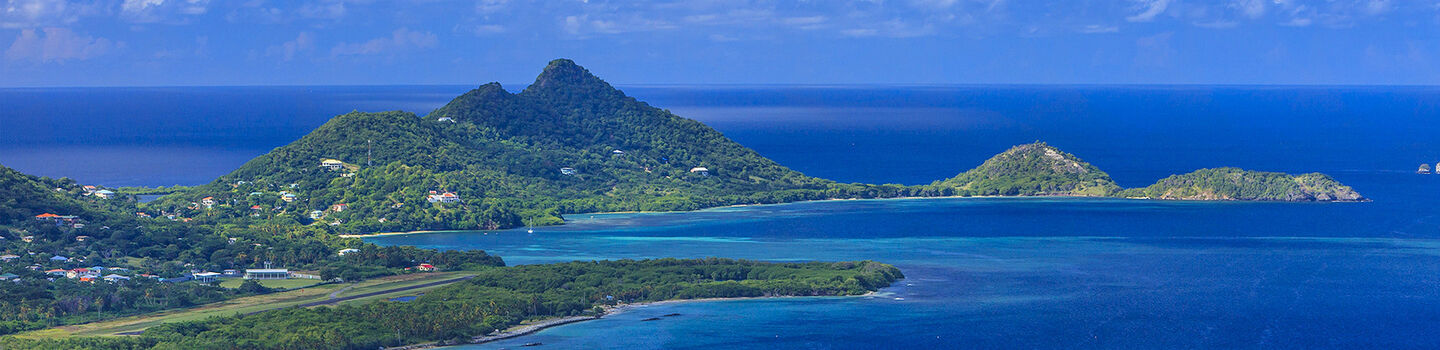 Von oben betrachtet, ragen die grüne Hügel Grenadas malerisch aus dem makellos blauen Meer, das nahtlos in den gleichermaßen blauen Horizont übergeht.