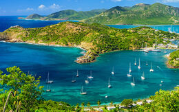 Das atemberaubende Luftbild zeigt die leuchtend grünen Landschaften von Antigua und Barbuda, umgeben vom tiefblauen Meer, in dem Boote malerisch verstreut sind.