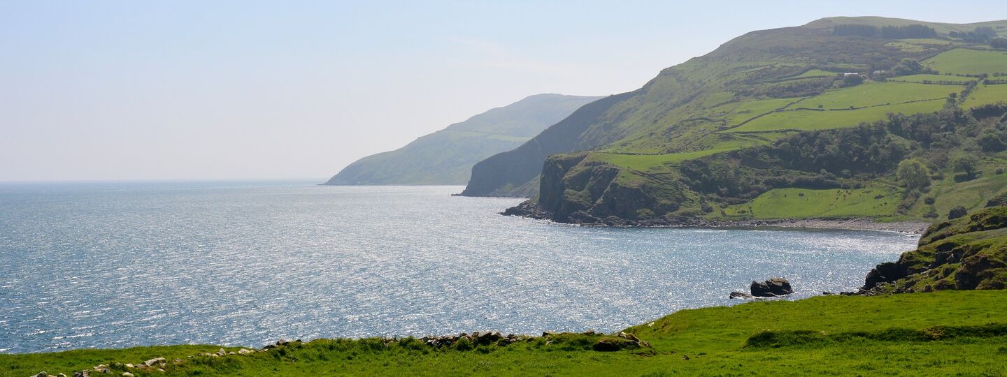 Blick von den Klippen in Cushendall (Irland) auf das Meer, mit sanften grünen Hügeln im Hintergrund