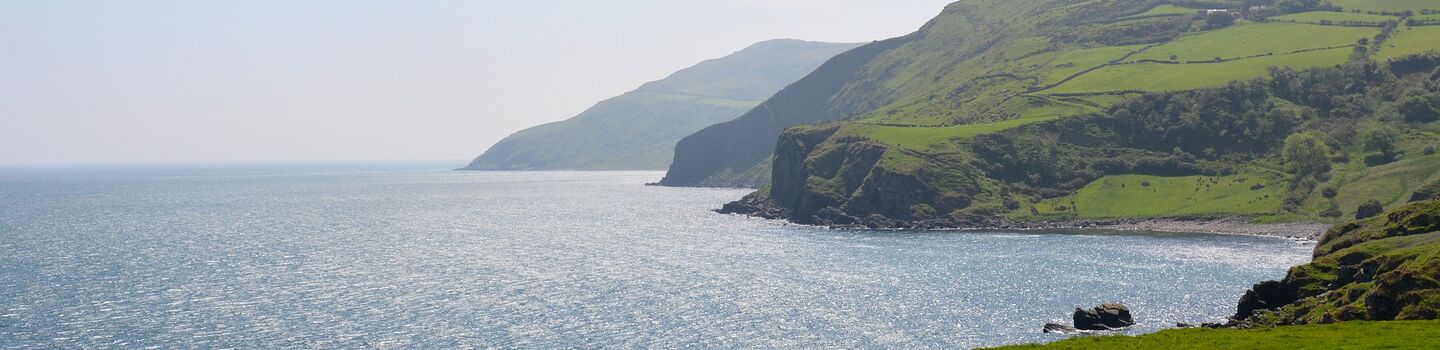 Blick von den Klippen in Cushendall (Irland) auf das Meer, mit sanften grünen Hügeln im Hintergrund