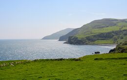 Blick von den Klippen in Cushendall (Irland) auf das Meer, mit sanften grünen Hügeln im Hintergrund