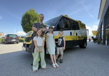Es ist ein Mann mit drei Kindern zu sehen, die vor einem ÖAMTC Pannenfahrzeug stehen.