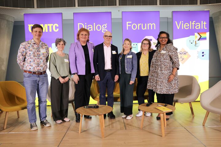 Auf dem Foto sind stehende Menschen auf einer Bühne zu sehen. Im Hintergrund sind Aufsteller mit dem Schriftzug "ÖAMTC Dialog Forum Vielfalt" zu sehen.