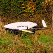 Eine Drohne des Projekts Medical Drone Service bei einem Testflug in Bodennähe, im Hintergrund sind man eine Wiese.