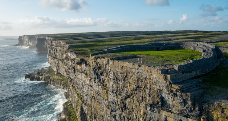 Das Foto zeigt die schroffe Steilküste der irischen Aran Islands mit grünen Wiesen und einer keltischen alten Siedlung Dun Aengu, Inishmore.