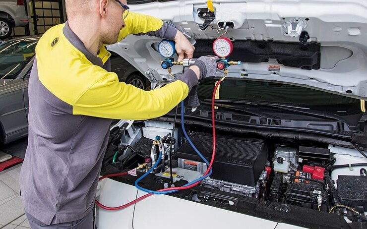 Ein ÖAMTC KFZ Techniker überprüft ein E-Auto in einer Werkstatt. Die Motorhaube ist geöffnet und ein Messgerät angeschlossen.