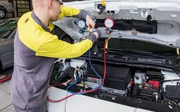 Ein ÖAMTC KFZ Techniker überprüft ein E-Auto in einer Werkstatt. Die Motorhaube ist geöffnet und ein Messgerät angeschlossen.