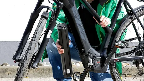 Eine Person kniet vor einem E-Bike und hält den E-Bike-Akku vom Fahrrad in der Hand.