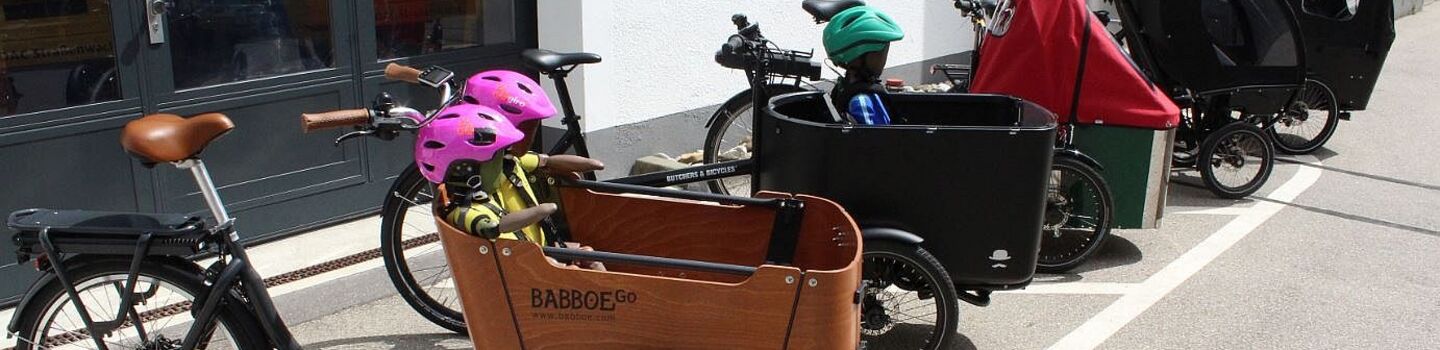 Fünf Elektro-Lastenfahrräder stehen aufgereiht vor einem Gebäude.