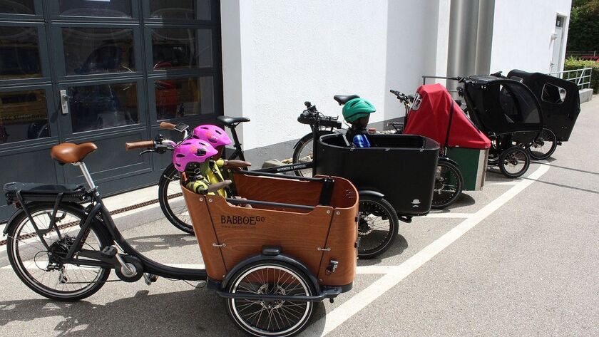 Fünf Elektro-Lastenfahrräder stehen aufgereiht vor einem Gebäude.