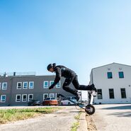 Ein Mann stürzt mit seinem E-Scooter über einen Bordstein.