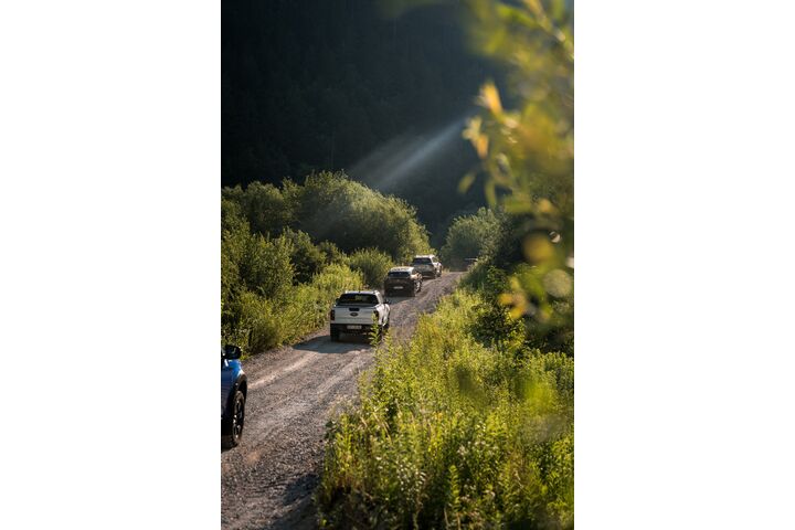 Im Bild ist eine Kolonne von Offroad-Fahrzeugen auf einer malerischen Schotterstraße unterwegs