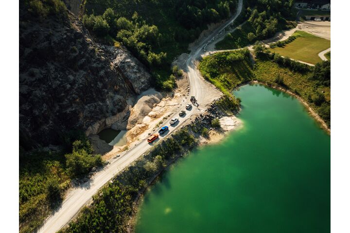 Luftaufnahme einer Kolonne von Offroad-Fahrzeugen im Offroad-Bereich der Experience World Saalfelden neben einem See