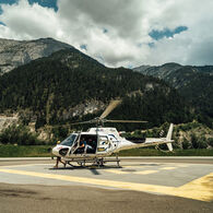 Im Bild ist der Hubschrauber der Experience World Saalfelden zu sehen, auf einem Landeplatz, vor einer malerischen Alpenkulisse