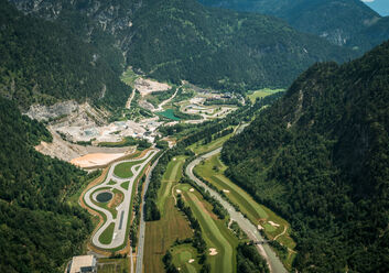 Luftaufnahme der Experience World Saalfelden - man sieht eine asphaltierte Rundstrecke, einen Offroad-Bereich, einen See und Teile eines Golfplatzes, mitten im Tal eines malerischen Alpenpanoramas