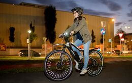 Eine junge Frau mit schwarzem Fahrradhelm fährt auf einem beleuchteten E-Bike in der Dämmerung. 