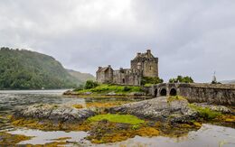 Malerischer Blick auf das Eilean Donan Castle in den schottischen Highlands bei Nebel, umgeben von Wasser und sanften Hügeln