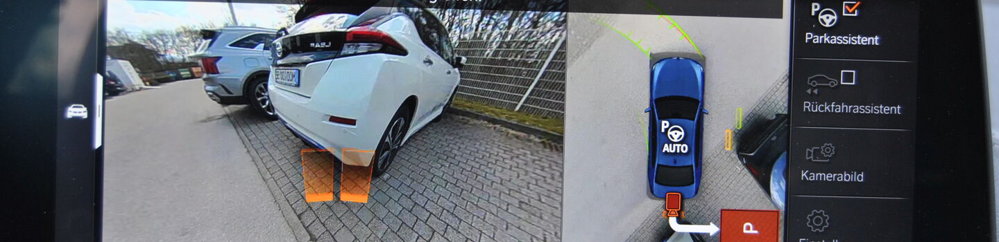 Screen von einem Einparkassistenten im Cockpit, darauf sichtbar das Heck von zwei Autos am Parkplatz.