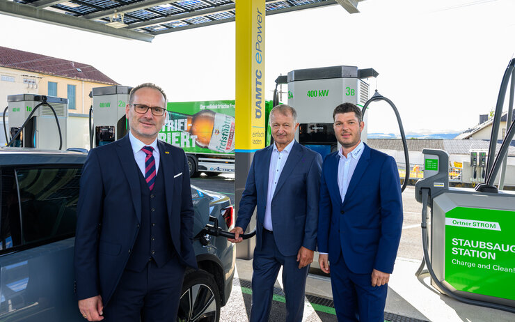 ÖAMTC ePower Business Auf dem Bild sind drei Männer in Anzügen zu sehen, die neben der neuen Ladestation stehen. Links im Bild ist Harald Großauer (Landesdirektor ÖAMTC Oberösterreich), er trägt einen dunklen Anzug mit Rot-schwarz-gestreifter Krawatte und eine Brille. Etwas weiter rechts im Bild stehen Franz Ortner und Michael Ortner (Eigentümer und Geschäftsführer Autohaus Ortner), beide tragen dunkelblaue Anzüge und hellblaue Hemden. Franz Ortner ist gerade dabei das Elektorauto aufzuladen.