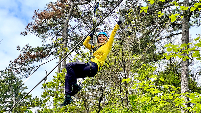 Eine Dame im Klettergarten ist gesichert an einem Seil zwischen den Bäumen.
