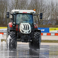 Im Bild ist ein Traktor zu sehen, der in einem Fahrtechnik Zentrum auf rutschigem Untergrund vor einem Wasserhindernis ausweicht
