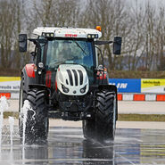 Im Bild ist ein Traktor zu sehen, der in einem Fahrtechnik Zentrum auf rutschigem Untergrund vor einem Wasserhindernis ausweicht
