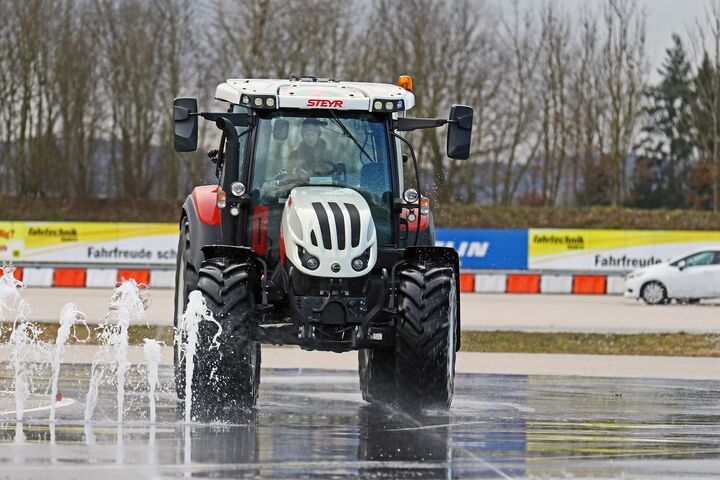 Im Bild ist ein Traktor zu sehen, der in einem Fahrtechnik Zentrum auf rutschigem Untergrund vor einem Wasserhindernis ausweicht