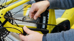 Ein ÖAMTC Techniker kontrolliert die Kette an einem gelben Fahrrad.