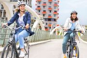 Zwei weibliche Personen fahren mit Fahrrädern über eine Brücke.