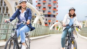 Zwei weibliche Personen fahren mit Fahrrädern über eine Brücke.