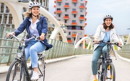 Zwei weibliche Personen fahren mit Fahrrädern über eine Brücke.