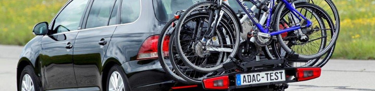Ein ADAC-Testauto fährt auf der Straße im Testgelände. Am Auto befindet sich ein Fahrradheckträger mit drei befestigten Fahrrädern darauf.