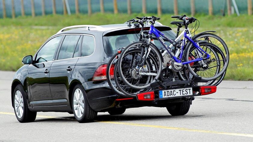 Ein ADAC-Testauto fährt auf der Straße im Testgelände. Am Auto befindet sich ein Fahrradheckträger mit drei befestigten Fahrrädern darauf.
