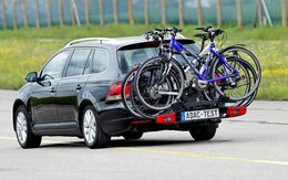Ein ADAC-Testauto fährt auf der Straße im Testgelände. Am Auto befindet sich ein Fahrradheckträger mit drei befestigten Fahrrädern darauf.
