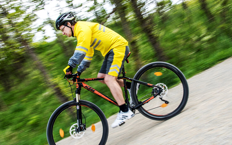 Ein Mann in Fahrraddress und Helm fährt mit dem Fahrrad auf einer Straße.