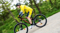 Ein Mann in Fahrraddress und Helm fährt mit dem Fahrrad auf einer Straße.