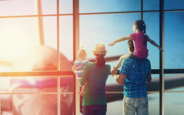 Eine Familie mit zwei Kindern schaut durch ein Flughafenfenster auf ein Flugzeug.