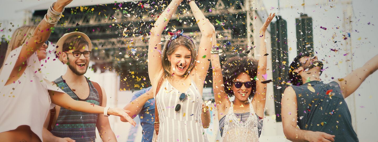 Eine Gruppe junger Menschen tanzt und feiert im Freien, umgeben von Konfetti.