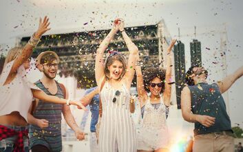 Festival Header-min.jpg Eine Gruppe junger Menschen tanzt und feiert im Freien, umgeben von Konfetti.
