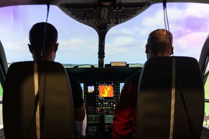 2 Personen sitzen im Cockpit des Flugsimulators und blicken auf eine Landschaft.