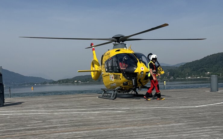 ÖAMTC-Flugrettung - Wasserrettung Christophorus-Hubschrauber steht auf einem Steg am See. Vor dem Hubschrauber geht ein Crew-Mitglied.