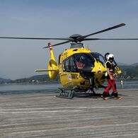 ÖAMTC-Flugrettung - Wasserrettung Christophorus-Hubschrauber steht auf einem Steg am See. Vor dem Hubschrauber geht ein Crew-Mitglied.