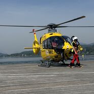 Christophorus-Hubschrauber steht auf einem Steg am See. Vor dem Hubschrauber geht ein Crew-Mitglied.