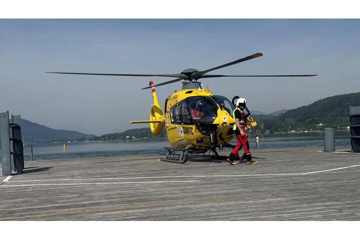 Christophorus-Hubschrauber steht auf einem Steg am See. Vor dem Hubschrauber geht ein Crew-Mitglied.