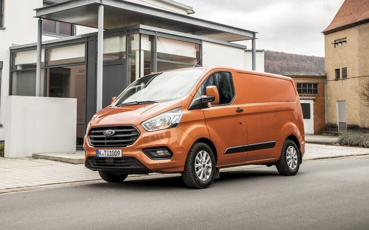 Das Bild zeigt ein orangenes Nutzfahrzeug vor einem Haus. 