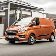 Das Bild zeigt ein orangenes Nutzfahrzeug vor einem Haus. 