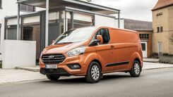 Das Bild zeigt ein orangenes Nutzfahrzeug vor einem Haus. 