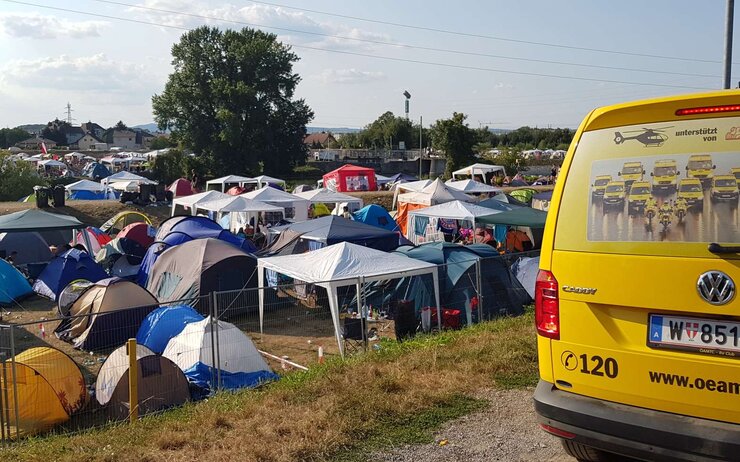 Frequency Festival 2018 Ein gelbes ÖAMTC Pannenfahrzeug steht neben mehreren Zelten auf einem Campingplatz in der Natur.